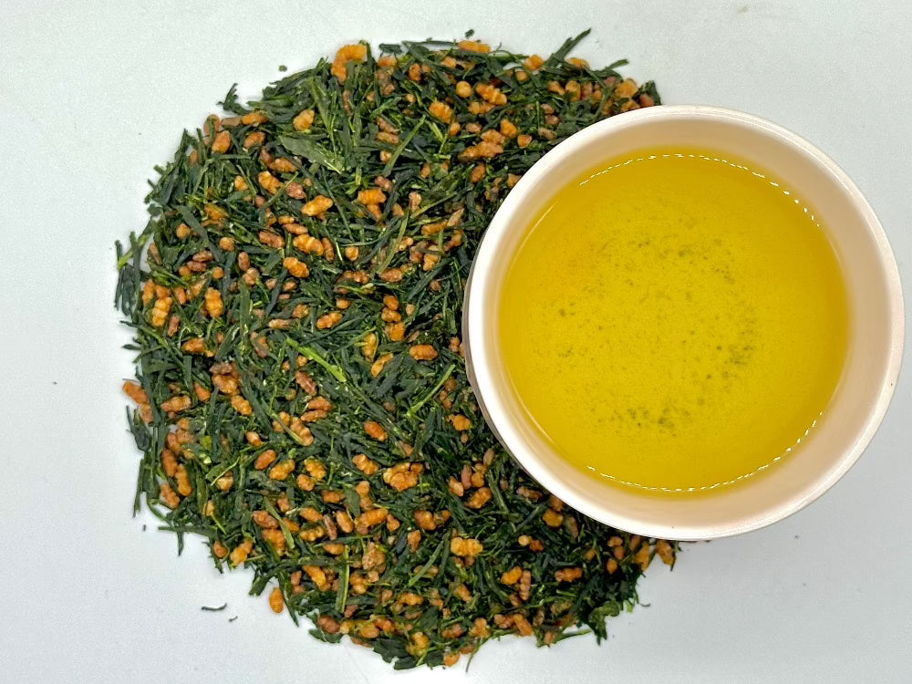 Loose leaf green tea mixed with roasted brown rice, with a cup of brewed tea beside it.