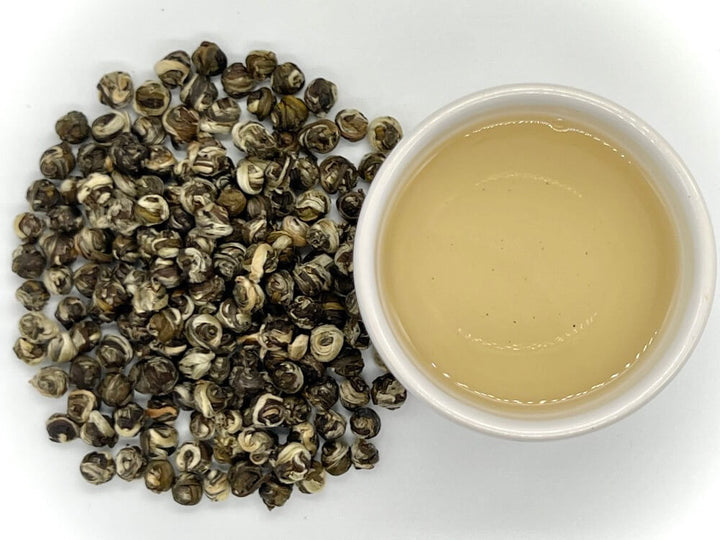 Tea leaves and a small bowl of tea broth on a white background