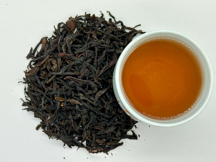 Black tea leaves and a cup of brewed tea on a white background