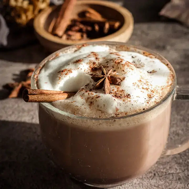 Hot chocolate with whipped cream, cinnamon stick, and star anise on a dark surface.